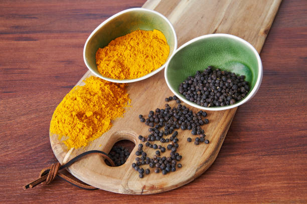 Poudre de curcuma et grains de poivre noir présentés dans des bols sur une planche en bois