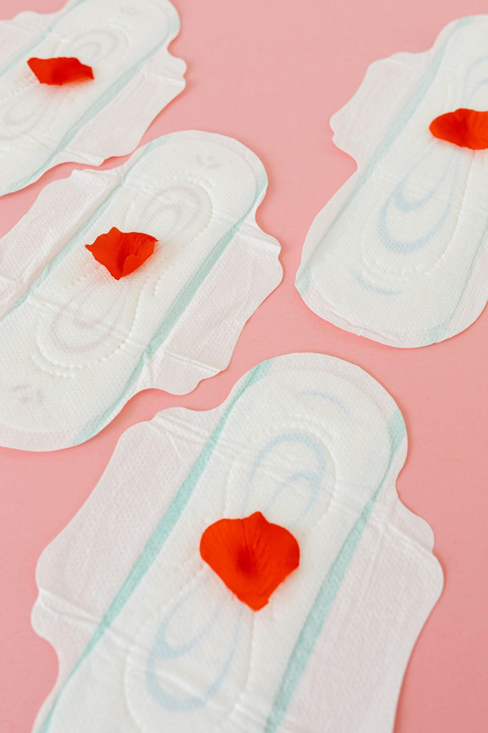 Texte alternatif : Serviettes hygiéniques avec pétales rouges illustrant le cycle menstruel et la santé féminine.