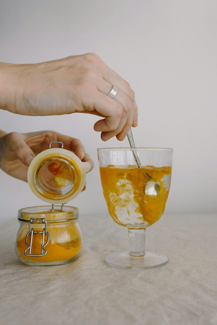 ain mélangeant une préparation de curcuma, citron et de gingembre dans un verre d'eau pour la recette de longévité de Kayla Barnes.