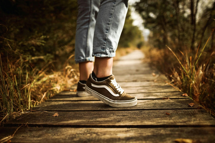 Gros plan des pieds d'une personne marchant d'un pas dynamique sur un sentier en bois en pleine nature, illustrant l'activité physique et la vitalité.