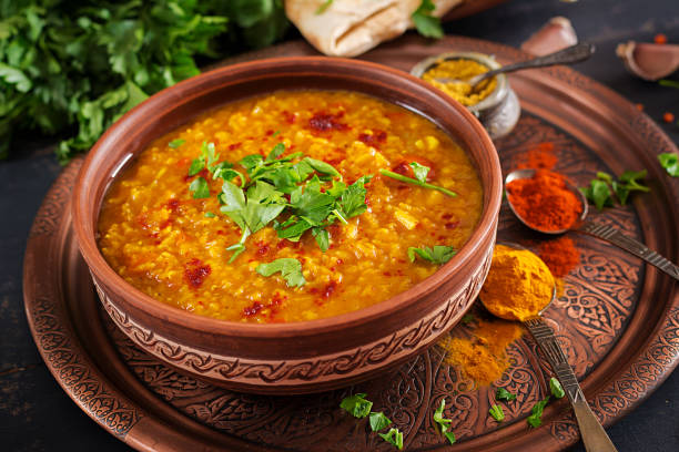 Dahl de lentilles corail au curcuma servi dans un bol en terre cuite, garni de persil frais et d’épices indiennes