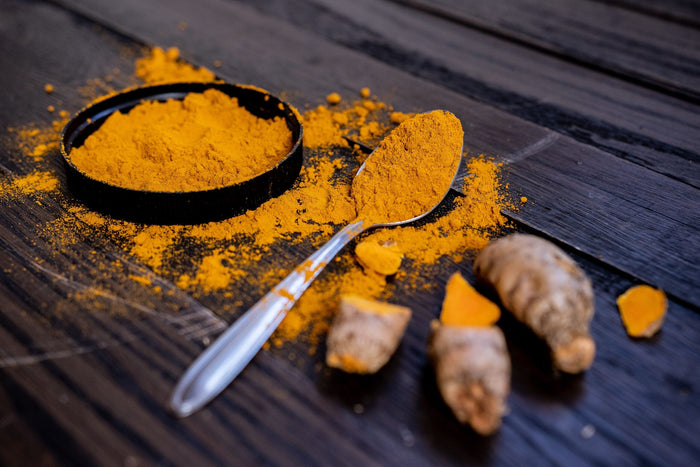 Rhizomes frais et poudre de curcuma orange dans une cuillère sur une table en bois.