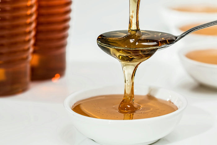 Miel doré et liquide versé d'une cuillère dans un bol blanc pour la préparation d'un remède naturel de phytothérapie à base de curcuma.