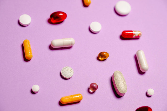 Compléments alimentaires variés, gélules et comprimés colorés disposés sur fond violet pour illustrer le choix entre curcuma et magnésium contre la fatigue